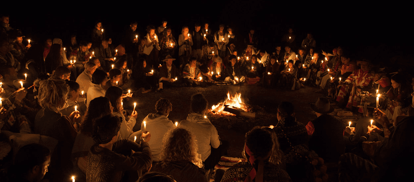 Community gathered in a circle at night around a fire, holding candles