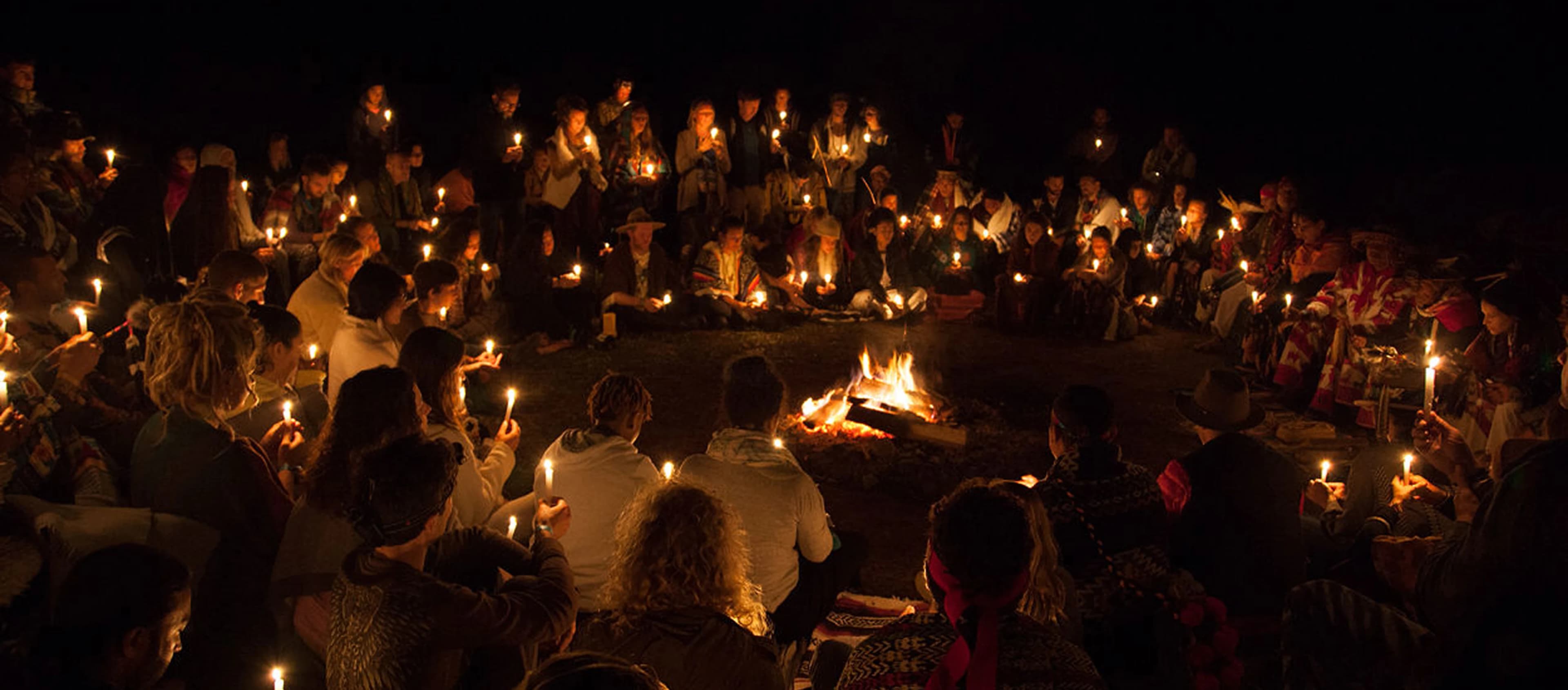 Community gathered in a circle at night around a fire, holding candles
