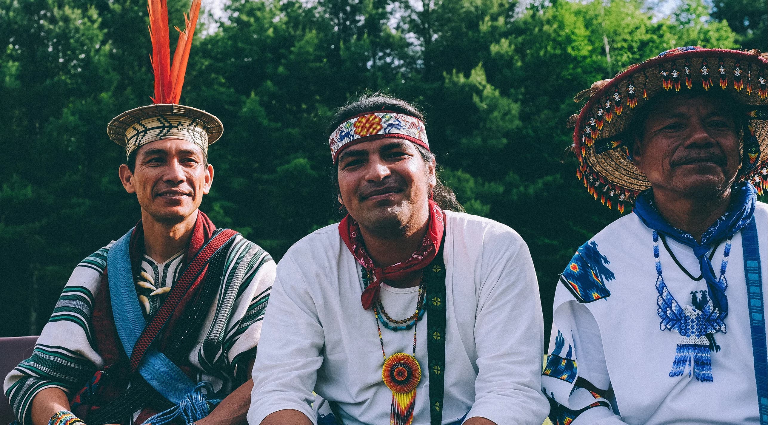 Indigenous elders and a community member in traditional regalia outdoors