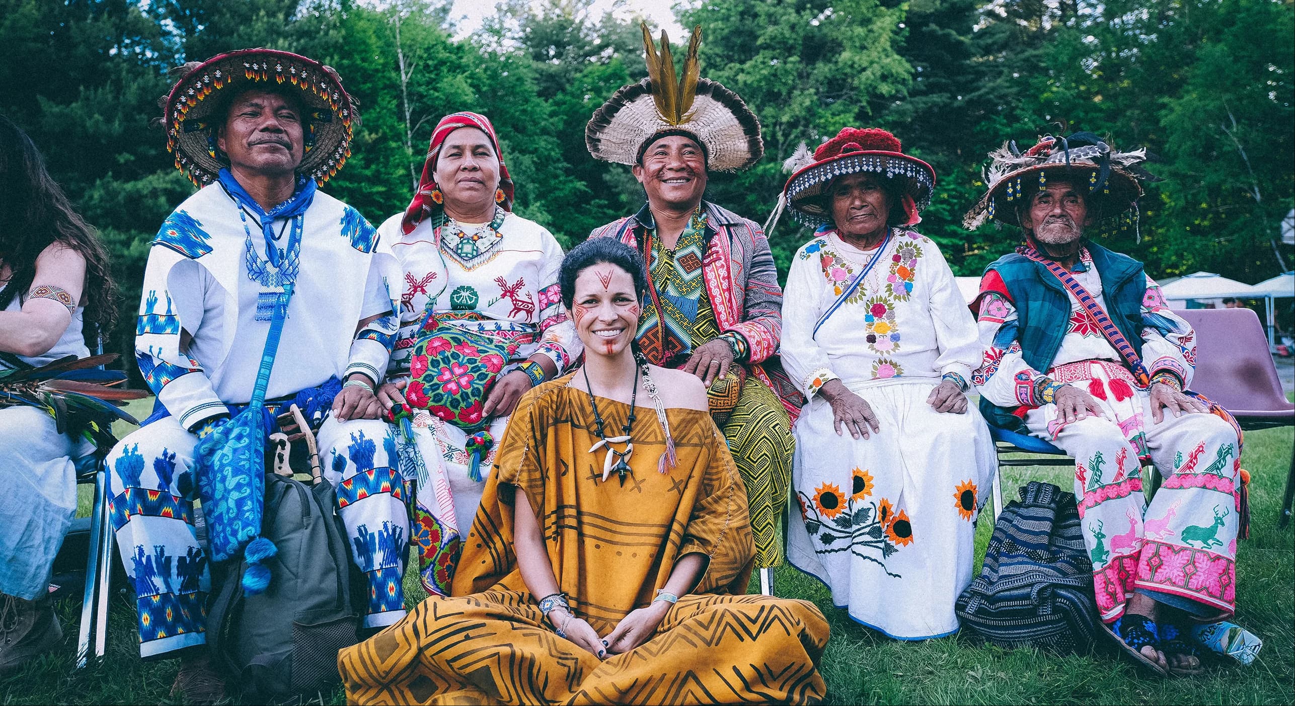 Indigenous elders and community members in traditional dress seated together outdoors